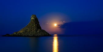 Moonrise over rocky sea stack in Sicily, Italy