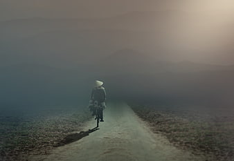 Lone Cyclist Riding on Misty Dirt Road Through Foggy Mountains