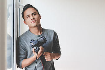 Young male photographer holding DSLR camera by window