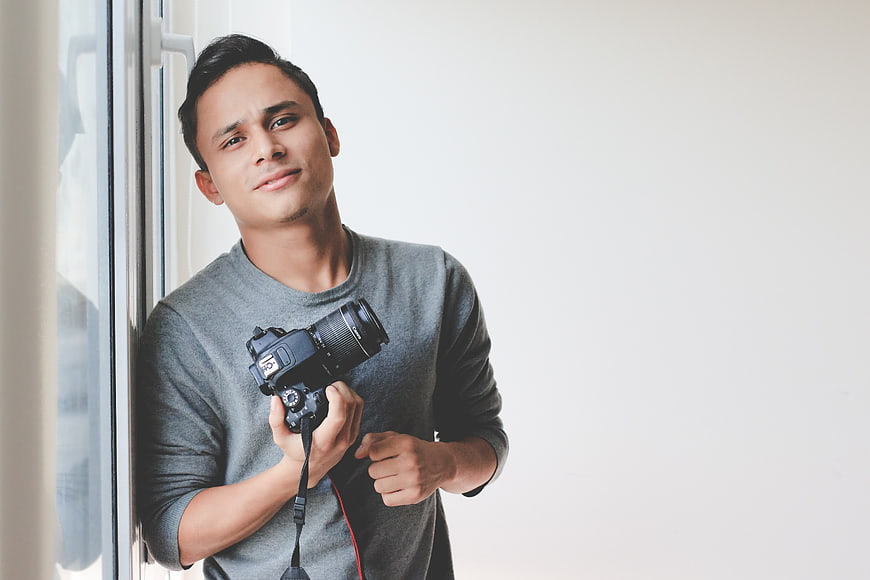 Young male photographer holding DSLR camera by window
