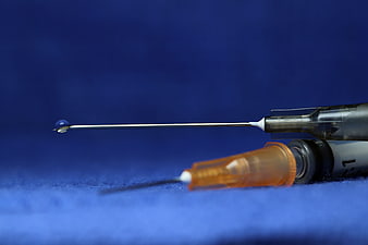 Close-up of medical syringe with liquid drop on blue background