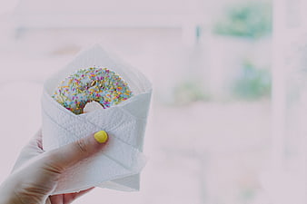 Hand holding glazed donut with sprinkles in napkin