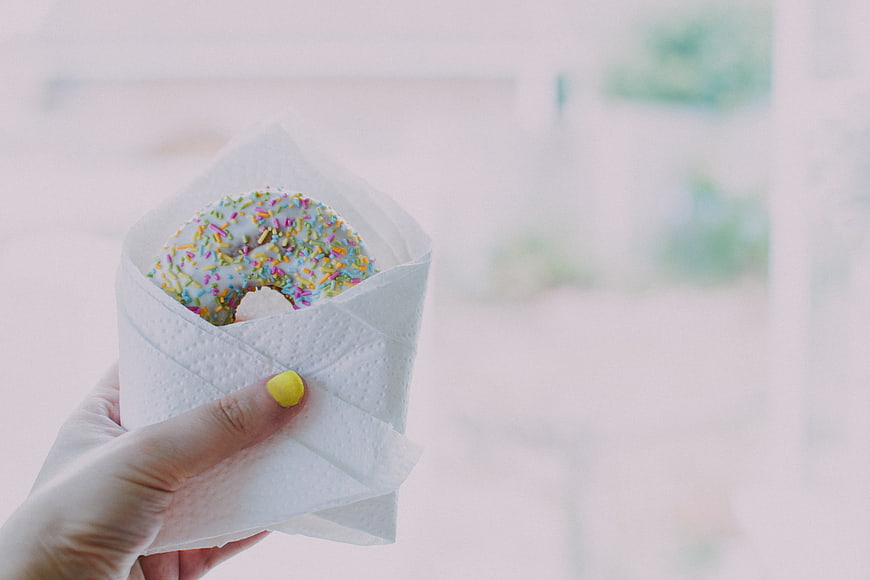 Hand holding glazed donut with sprinkles in napkin