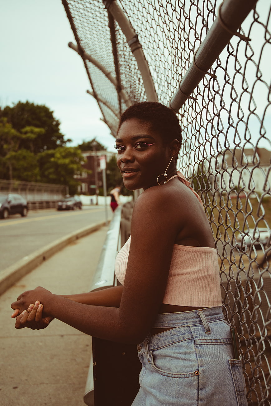 Stylish Black Woman Leaning on Chain Link Fence in Urban Setting