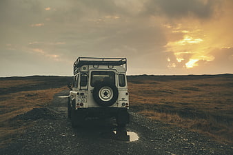 White Land Rover Defender on Gravel Road at Sunset