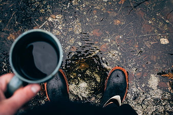 First-person view of coffee mug and boots in shallow water