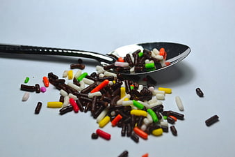 Colorful Chocolate Sprinkles Spilling From A Spoon On White Background