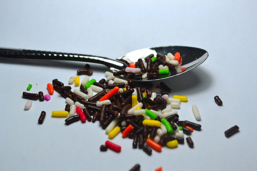 Colorful Chocolate Sprinkles Spilling From A Spoon On White Background