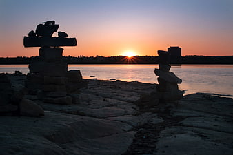 Silhouetted Rock Cairns on Rocky Shore at Sunset