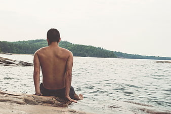 Man Sitting on Rocks by the Sea Looking at Water