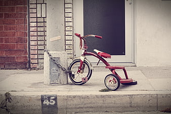 Vintage red tricycle chained to concrete post on sidewalk
