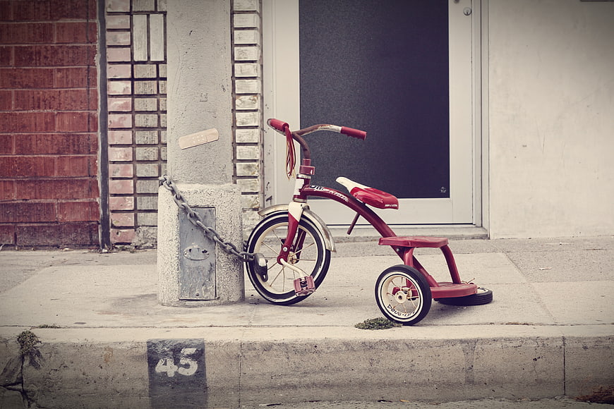 Vintage red tricycle chained to concrete post on sidewalk