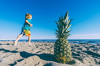 Child Running Past Giant Pineapple on Sandy Beach