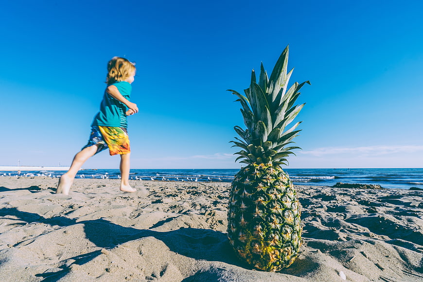 Child Running Past Giant Pineapple on Sandy Beach