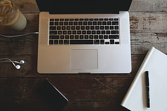 Flat lay of laptop, iced coffee, and notebook on wooden desk