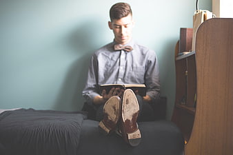Young man in bow tie reading book on bed in bedroom