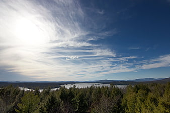 Wide landscape view of forest, lake, and mountains under blue sky