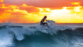 Surfer riding a wave during a vibrant orange sunset