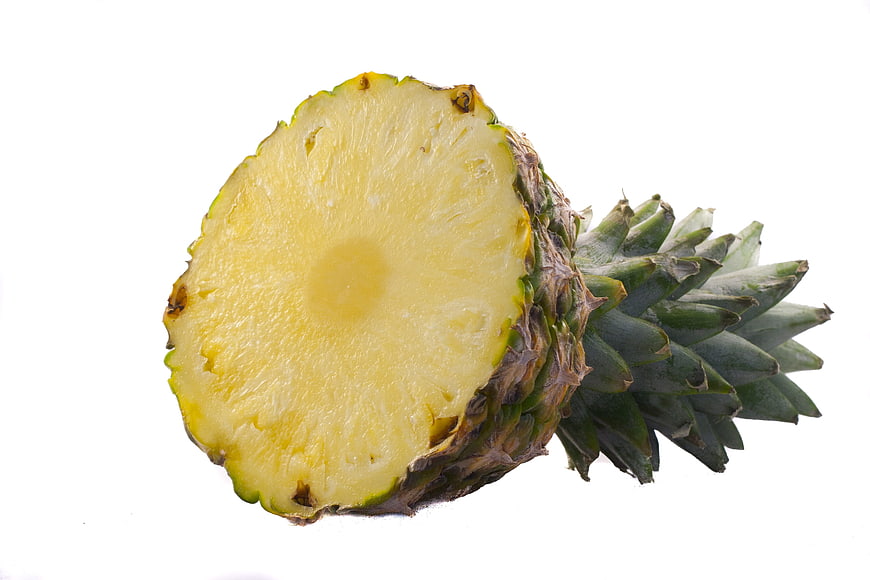 Cut pineapple slice with green crown on white background