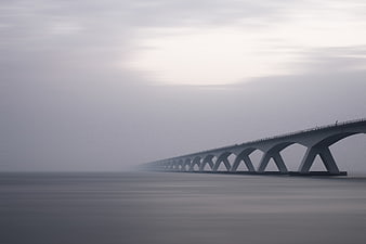 Long concrete bridge disappearing into fog over calm water