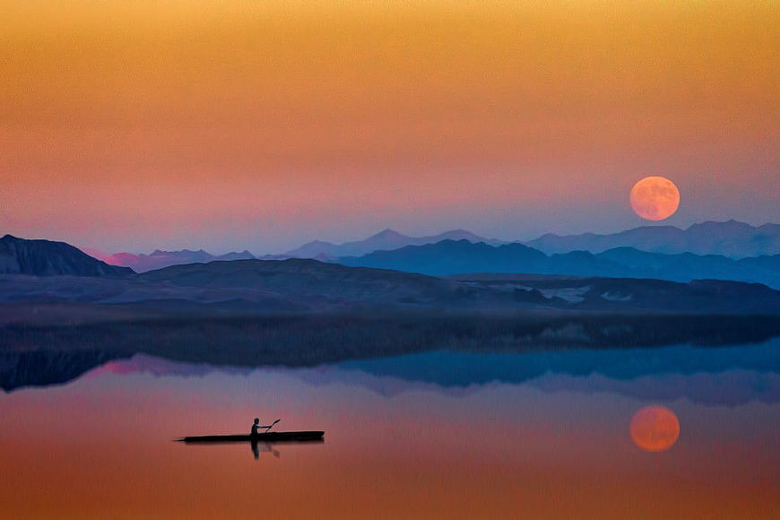 Silhouette of Man Kayaking on Lake at Sunset with Moon