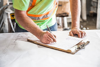 Construction worker writing on clipboard over blueprints