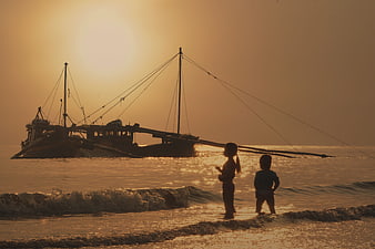 Silhouetted children on beach at sunset with fishing boat