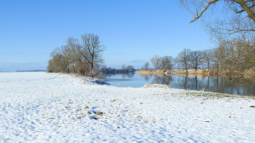 Serene Winter Landscape with Snowy Riverbank and Blue Sky