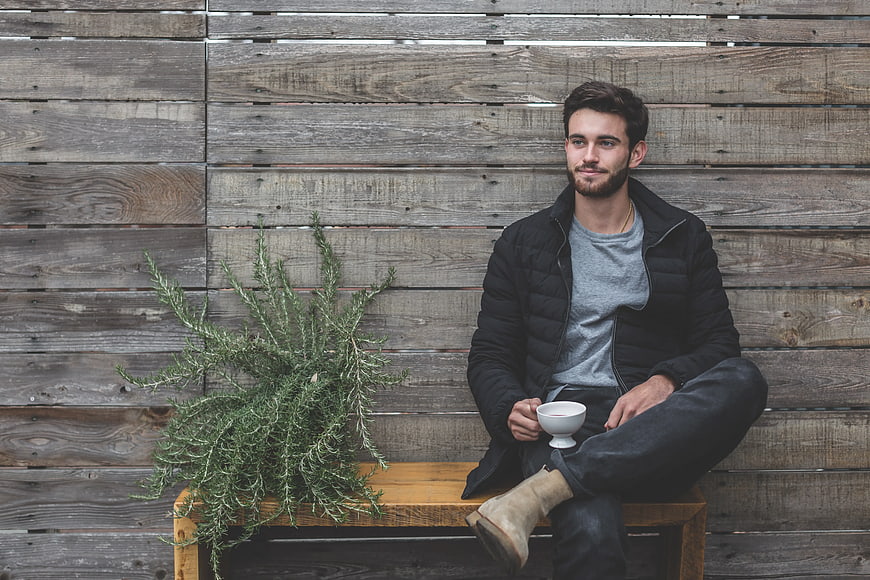 Man Sitting on Wooden Bench with Coffee and Plant
