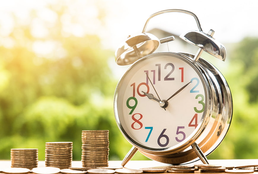 Alarm Clock and Stacks of Coins on Wooden Table