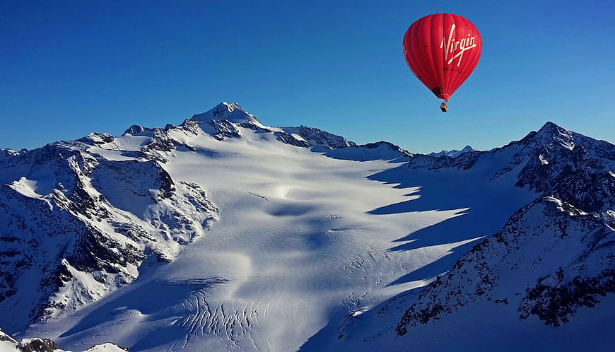 Red Virgin Hot Air Balloon Flying Over Snowy Alpine Glacier