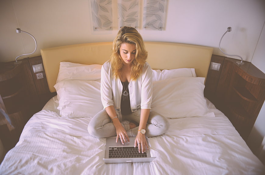 Young woman working on laptop sitting on bed