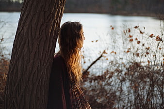 Woman leaning against tree by lake in autumn