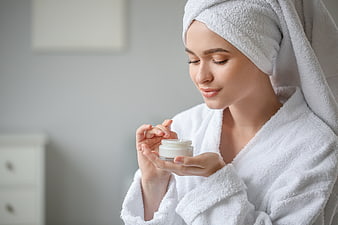 Woman in white robe holding skincare cream jar