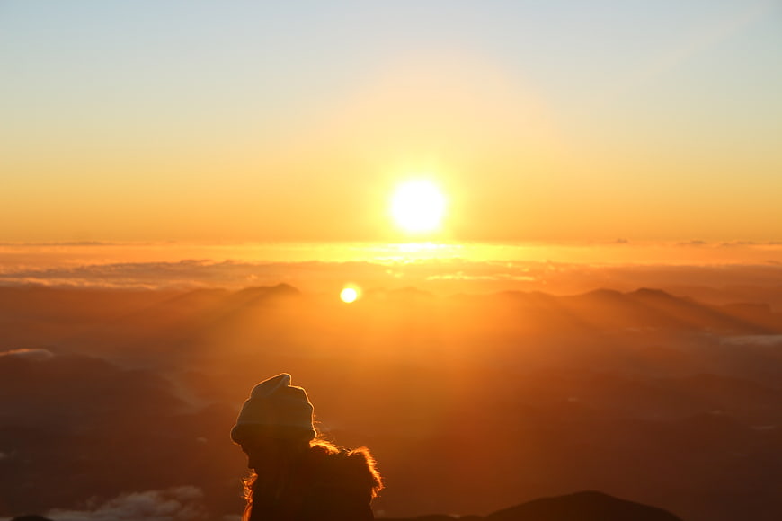 Silhouette of hiker watching sunrise over mountain clouds
