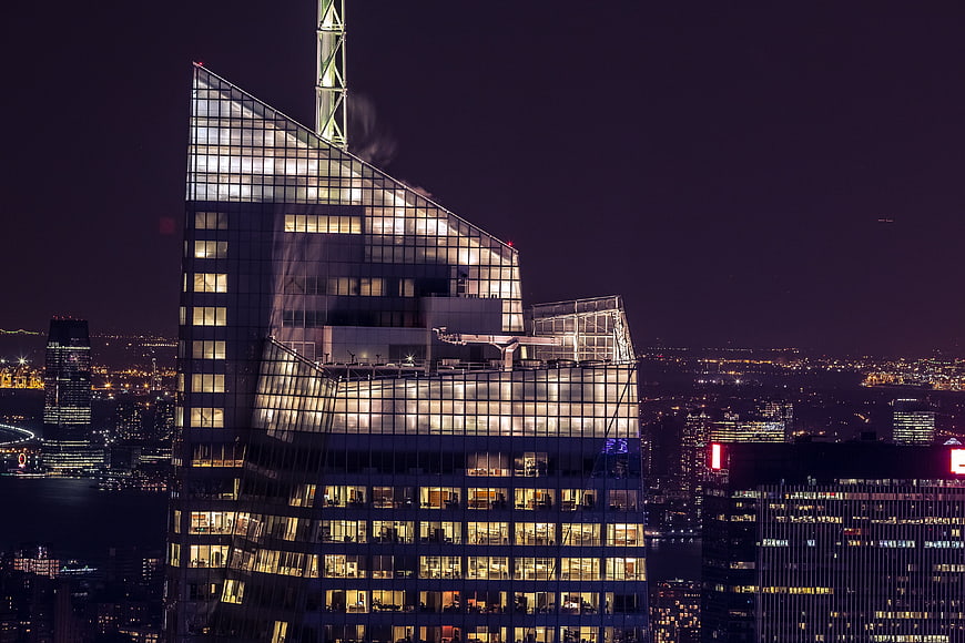 Illuminated modern skyscraper at night with city skyline background