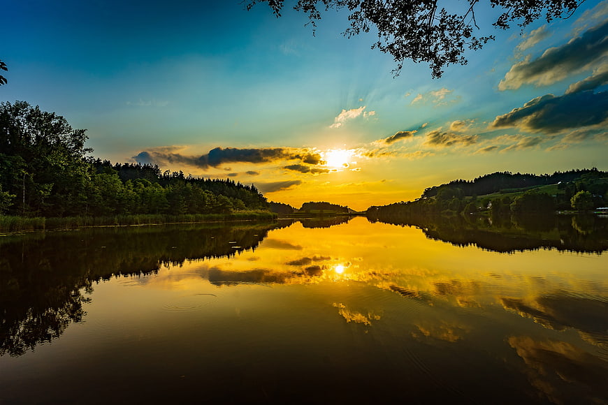 Golden Sunset Reflection on a Calm Lake with Forested Hills