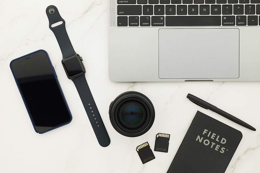 Flat lay of photography gear, laptop, and smartwatch on marble