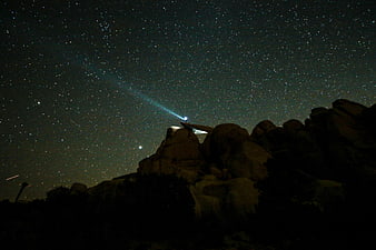 Night sky with stars and flashlight beam over rocky landscape
