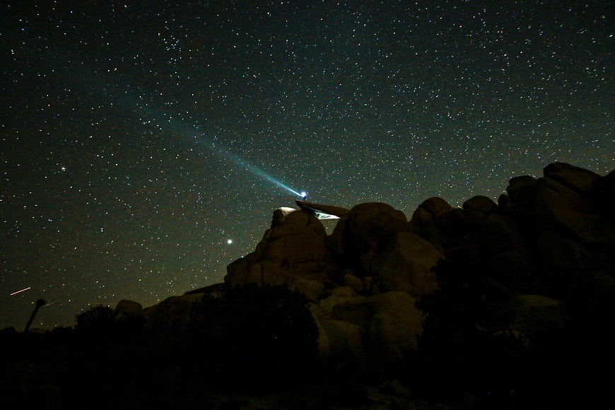 Night sky with stars and flashlight beam over rocky landscape