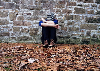 Lonely boy sitting against stone wall in autumn leaves
