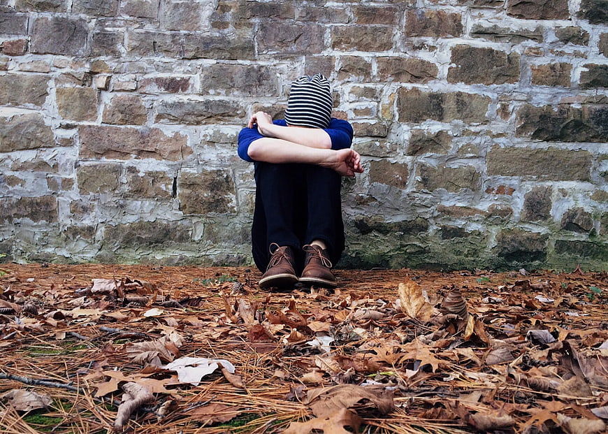 Lonely boy sitting against stone wall in autumn leaves