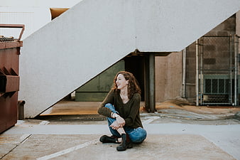 Happy woman sitting under concrete staircase in urban alley
