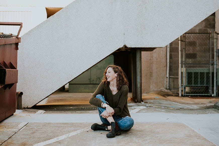 Happy woman sitting under concrete staircase in urban alley