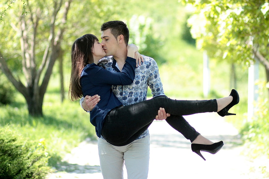 Romantic couple kissing in park with man carrying woman