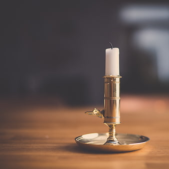 Unlit white candle in brass holder on wooden table