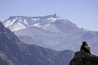 Hiker sitting on rock overlooking snow-capped mountain peak