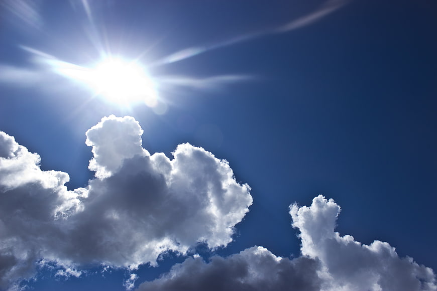Bright Sun Shining Through White Clouds in Blue Sky