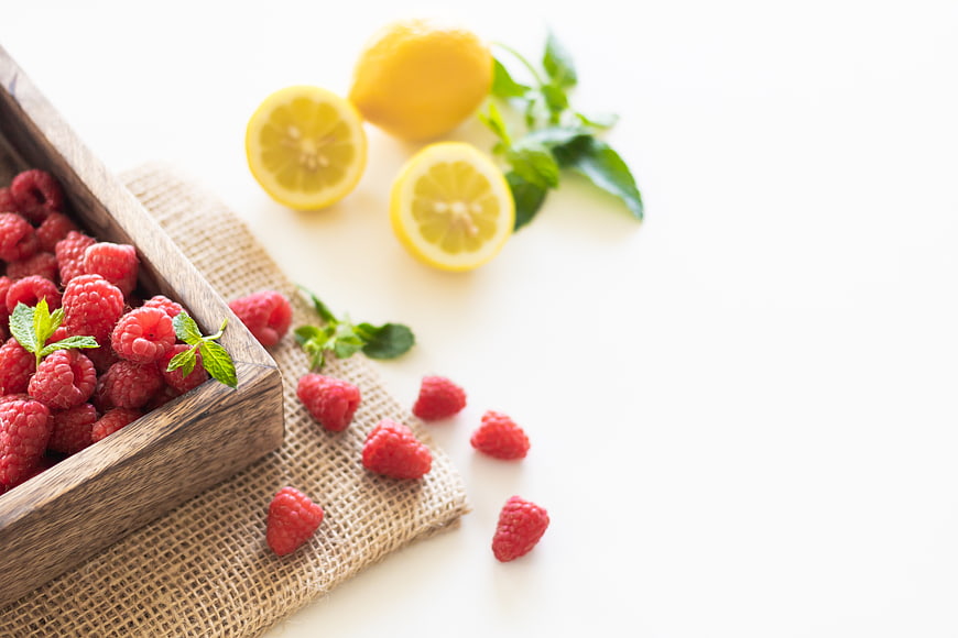 Fresh Raspberries and Lemons on White Background with Copy Space