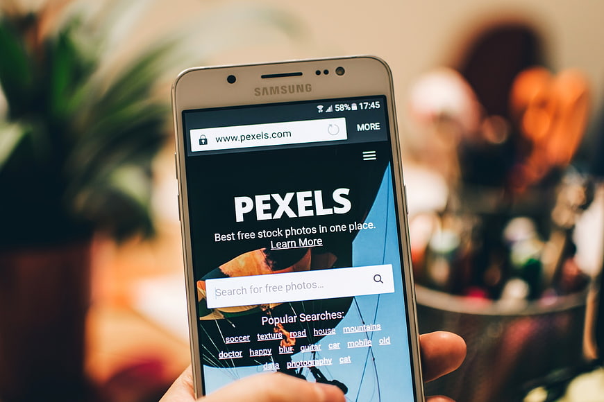 Hand holding smartphone displaying Pexels stock photo website
